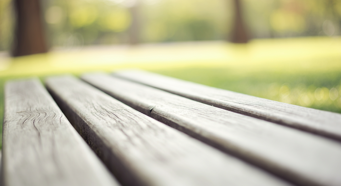 パステルカラーの柔らかな光が当たる公園のベンチのクローズアップ写真。背景は緑にぼけている。